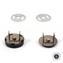 Zwei Metall-Unterlegscheiben und zwei schwarze Druckknopf-Rückseiten mit sichtbaren Metallzapfen zur Befestigung im Stoff.