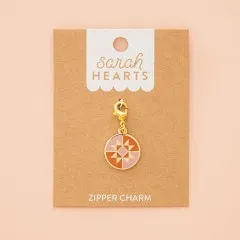 Zipper Charm auf Verpackungskarte, fotografiert vor zartrosa Hintergrund.