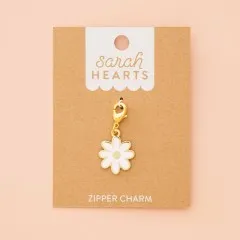 Gänseblümchen-Zipper-Charm auf Verpackungskarte, fotografiert vor zartrosa Hintergrund.
