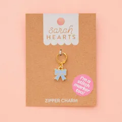 Zipper Charm auf Verpackungskarte, fotografiert vor zartrosa Hintergrund.