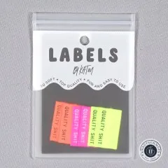 Verpackungskarte „Labels by KATM" mit den „Quality Shit"-Labels in Neongelb, Neonorange und Knallpink, gerade von vorne fotografiert.