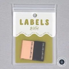 Verpackungskarte „Labels by KATM" mit den „You Can't Buy This"-Labels in Schwarz und Kamel, gerade von vorne fotografiert.