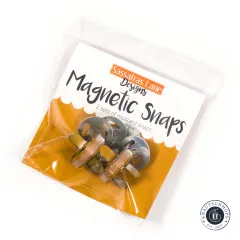 Originalverpackung der Sassafras Lane Magnetic Snaps in Mustard, schräg fotografiert mit sichtbaren Druckknöpfen und Scheiben im Beutel.