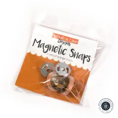 Originalverpackung der Sassafras Lane Magnetic Snaps in Orange, schräg fotografiert mit sichtbaren Druckknöpfen und Scheiben im Beutel.