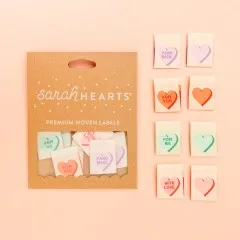 Kraftpapier-Verpackung „Valentines" neben acht cremefarbenen Weblabels mit Bonbonherzen und Sprüchen „Hand Made", „For You", „For Me" und „With Love" in Lavendel, Orange, Mint und Rosa.