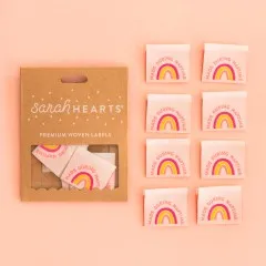 Kraftpapier-Verpackung „Made during Naptime" neben acht rosafarbenen Weblabels mit Regenbogen in Pink, Koralle und Gelb.
