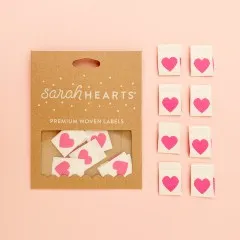 Kraftpapier-Verpackung „Pink Heart" neben acht cremefarbenen Weblabels mit pinkfarbenem Herz.