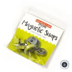 Originalverpackung der Sassafras Lane Magnetic Snaps mit dem Hinweis „2 sets of wasabi snaps", schräg fotografiert mit Blick auf die gelbgrünen Druckknopf-Teile.