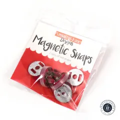 Originalverpackung der Sassafras Lane Magnetic Snaps mit dem Hinweis „2 sets of red snaps", schräg fotografiert mit Blick auf die roten Druckknopf-Teile.