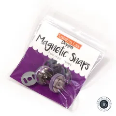 Originalverpackung der Sassafras Lane Magnetic Snaps mit dem Hinweis „2 sets of purple snaps", schräg fotografiert mit Blick auf die violetten Druckknopf-Teile.