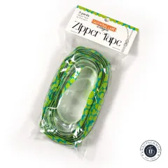 Schräg aufgenommene Verpackung 'Zipper Tape' von Sassafras Lane Designs mit oval aufgerolltem Lime-Pebble-Band im Beutel.