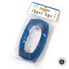 Schräg aufgenommene Verpackung 'Zipper Tape' von Sassafras Lane Designs mit oval aufgerolltem Blue-Pebble-Band im Beutel.