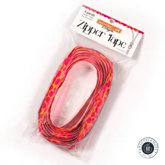 Schräg aufgenommene Verpackung 'Zipper Tape' von Sassafras Lane Designs mit oval aufgerolltem Pink-Pebble-Band im Beutel.