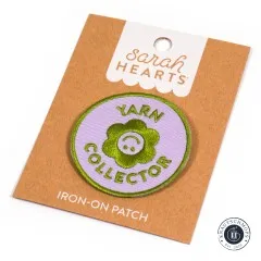 Sarah Hearts Iron-On Patch „Yarn Collector" mit Blüten-Smiley auf lila Rundpatch, schräg auf der Verpackungskarte fotografiert.
