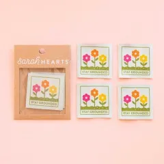 Verpackung neben vier ausgelegten Stay-Grounded-Weblabels mit Blumenmotiv.