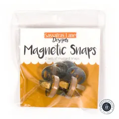 Vorderseite der Verpackung 'Magnetic Snaps' von Sassafras Lane Designs mit Aufschrift '2 sets of mustard snaps'.