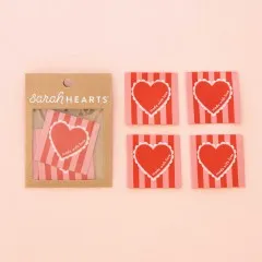 Vier gestreifte „Made with Love“-Labels mit rotem Herzmotiv ausgelegt auf rosa Hintergrund.