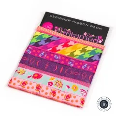 Verpackung des Tula-Pink-Webband-Sets „Untamed" in Cosmic mit sieben unterschiedlich breiten Bändern in Pink-, Orange- und Lilatönen.