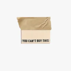 Einzelnes Creme-Label You Can't Buy This mit schwarzer Schrift, mittig gefaltet mit Klebeband fixiert