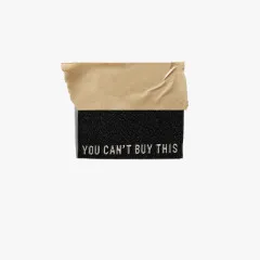 Einzelnes schwarzes Label You Can't Buy This mit cremefarbener Schrift, mittig gefaltet mit Klebeband fixiert