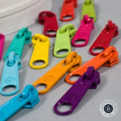 Sechzehn bunte XL-Zipper-Anhänger auf grauem Stoffuntergrund