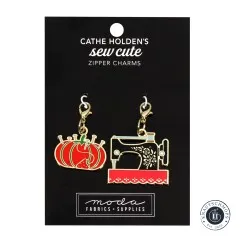 Zwei goldene Emaille-Anhänger von Cathe Holden: eine Nähmaschine und ein rotes Tomaten-Nadelkissen, auf Verpackungskarte.