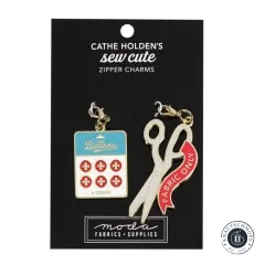 Zwei goldene Emaille-Anhänger von Cathe Holden: eine Schere und eine Knopf-Karte, auf Verpackungskarte, schräge Ansicht.
