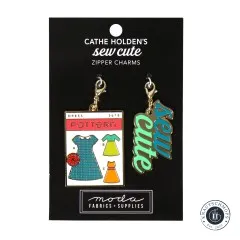 Zwei goldene Emaille-Anhänger von Cathe Holden: eine Kleider-Schnittmusterpackung und der Schriftzug 'sew cute', auf Verpackungskarte.