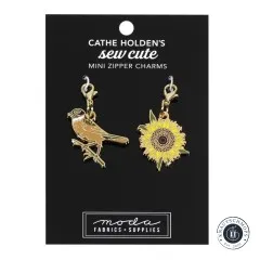 Zwei goldene Emaille-Anhänger von Cathe Holden: ein Vogel und eine Sonnenblume, auf Verpackungskarte.