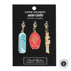 Drei goldene Emaille-Anhänger von Cathe Holden mit den Schriftzügen 'Wildflower', 'Bloom' und 'Lovely', auf Verpackungskarte.