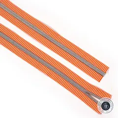 Zwei diagonal ausgelegte Längen des orange-weiß gestreiften Reißverschlussbandes mit silberner Zahnreihe auf weißem Hintergrund.