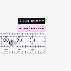 Labels 'I Didn't Fuck It Up' in Schwarz und Rosa mit Lineal zum Größenvergleich.